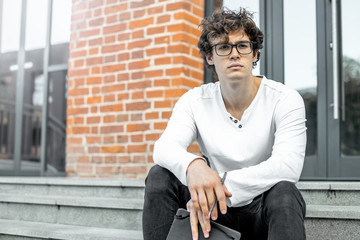 Close up of pensive man sitting on concrete steps and holding notepad in hands.