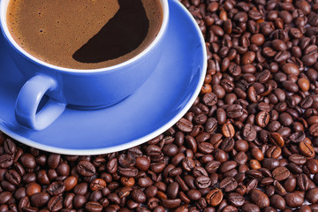 Coffee in blue cup on a table surrounded by coffee beans. Coffee in the shape of a smile