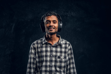 Handsome black guy in headphones standing,smiling and posing in studio on black background