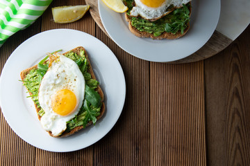 Sandwich or bread toast with avocado and a fried egg on a white plate on rustic wood table. Healthy food. Healthy eating.