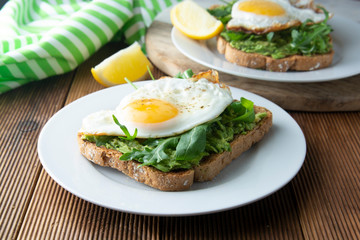 Sandwich or bread toast with avocado and a fried egg on a white plate on rustic wood table. Healthy food. Healthy eating.