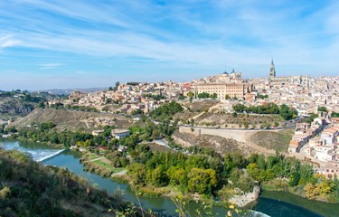 Fototapeta na wymiar A panoramic view of the old city of Toledo, with it’s defensive walls and the tower of the cathedral inside the city walls, surrounded by a ravine and river that serves as a moat.