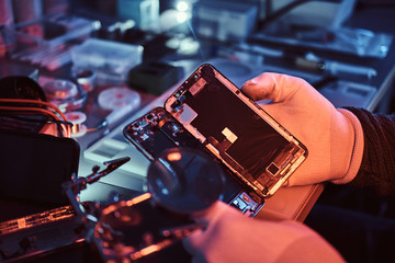 Fototapeta na wymiar The technician carefully examines the integrity of the internal elements of the smartphone in a modern repair shop. Illumination with red and blue lights