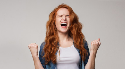 Overjoyed young redhead woman screaming with joy