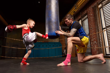 Trainer teaching a kid how to hit punches. Kid wearing boxing gloves and head guard training with his coach inside a boxing ring