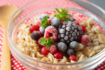 Healthy breakfast in a bowl with oatmeals, frozen berries, fresh strawberries, mint. Oat porridge with fruits.