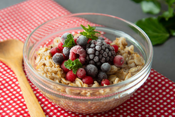 Healthy breakfast in a bowl with oatmeals, frozen berries, fresh strawberries, mint. Oat porridge with fruits.