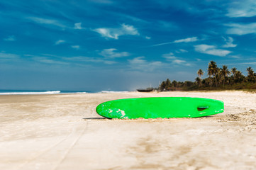 Surfboard on a tropical beach overlooking the ocean, blue sky background. Colored Board for surfing on the sand.