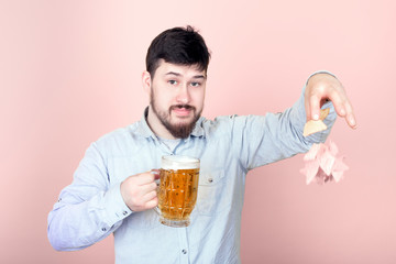 cute bearded man with a glass of beer drops nachos, image on a pink background