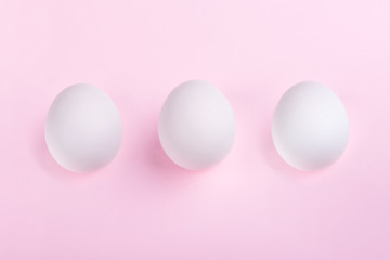 three white eggs on pastel pink background, concept Happy Easter
