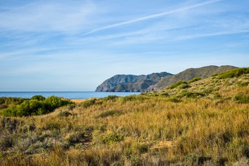 A grassy field leads to the beach with the blue water of the Mediterranean and a distant cliff on the edge of the water