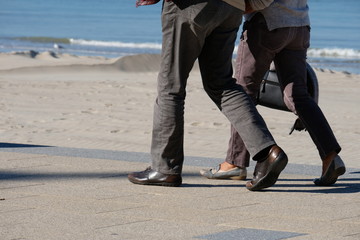 Obraz premium legs of a man and a woman walking in trousers and shoes along the promenade against the sea