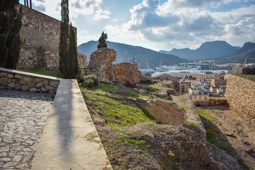 Ancient walls stretch out towards the modern harbour of Cartagena, Spain and the town below, with dark mountains on the horizon. 