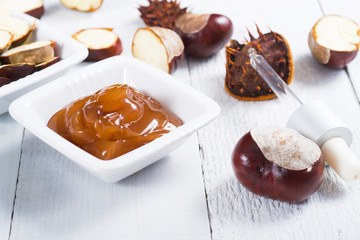medicine cream, ground conkers tincture with alcohol and sliced seeds from horse chestnuts, on white wooden table