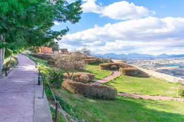 The gardens of Lorca Castle in southern Spain, showing walkways that cris-cross the lawn, with a wall on the far-side and the view down below.