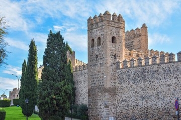 Fototapeta na wymiar The defensive stone walls of Toledo, Spain, showing the battlements on top and a guard tower with the green lawn that now surrounds the city.