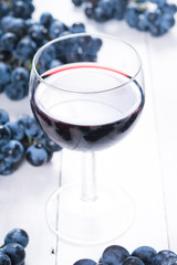 glass of red wine and blue grapes on white wooden table background