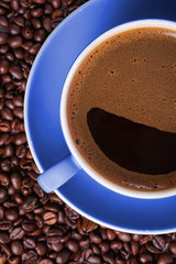 Coffee in blue cup on a table surrounded by coffee beans. Coffee in the shape of a smile