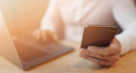 Man's hands using smart phone and laptop in interior.