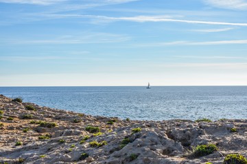 The dry semi-desert of southern Spain meets the blue water of the mediterranean with rocks rising above the water and a small sailboat sailing, along the coast.