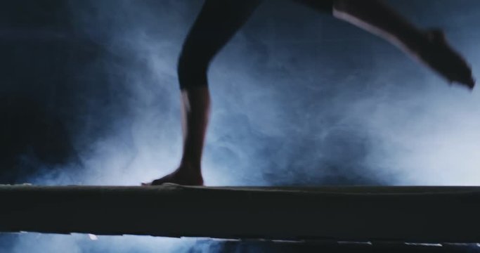 Legs Professional girl gymnasts jump in slow motion in the smoke on the balance beam. Women's Artistic Gymnastics