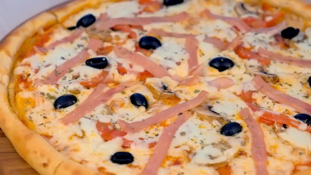 Cook cuts pizza with bacon and cheese on wooden board on the table. Close-up view.