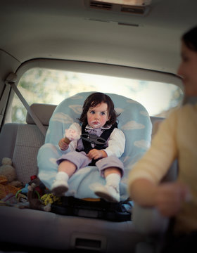 Young girl sitting with ice cream around her mouth in a carseat in the back of her mother's car.