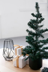 A small Christmas tree and Christmas gifts in a package with a gold ribbon on a wooden table
