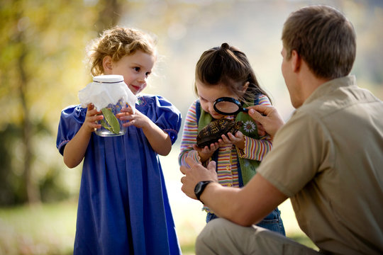 Girl with magnifying glass examining a turtle with her father.