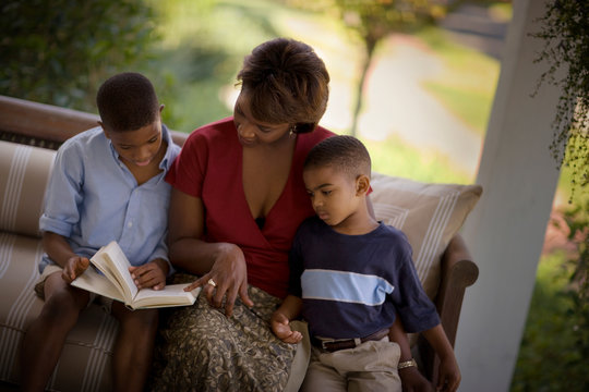 Mid-adult woman sitting on a couch reading with her two sons.