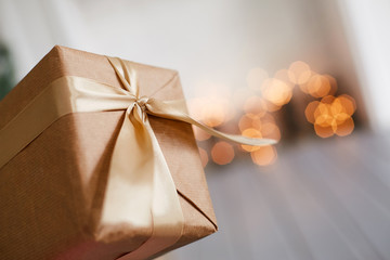 Gift packaging brown tied with a gold ribbon with a bow. Blurred background with lights