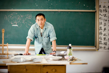 Portrait of a young adult man standing near a chalk board in a classroom.