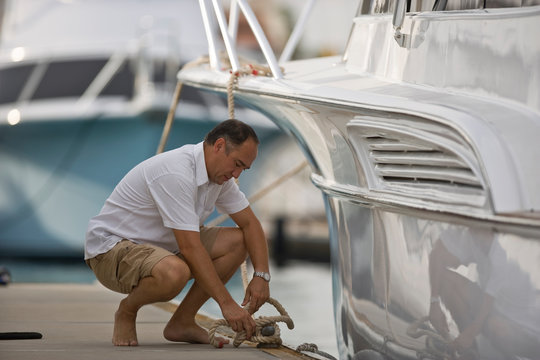 Mature man crouching while untying his boat from a wooden jetty.