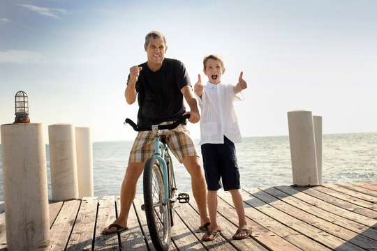 Portrait of a smiling father and his son with a bicycle on a wharf.