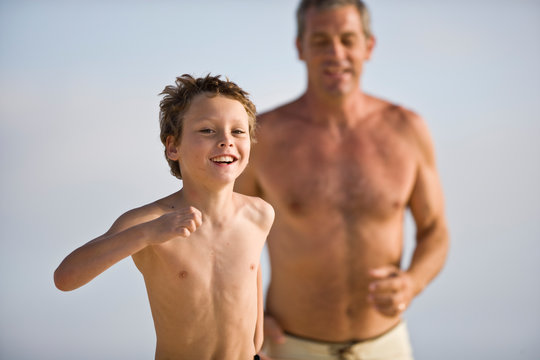 Portrait of a boy running along a beach being chased by his mid-adult father.