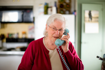 Senior woman speaking into a telephone inside her kitchen.