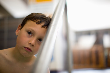 Young boy leaning head against swimming pool railing