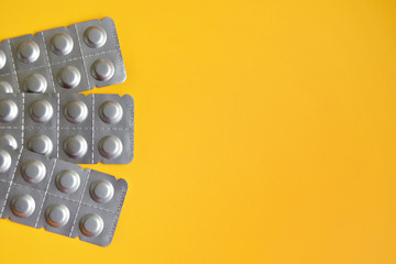 Round medical tablets in three packs, tablets packed in blisters on the left side with copyspace on yellow background