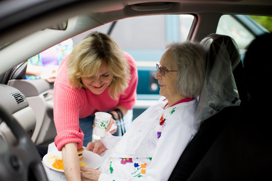 Mid-adult woman reaching over her elderly mother who is sitting inside a car.