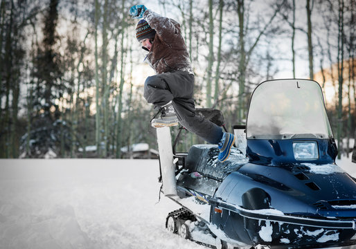 Happy young boy leaping off a snowmobile.