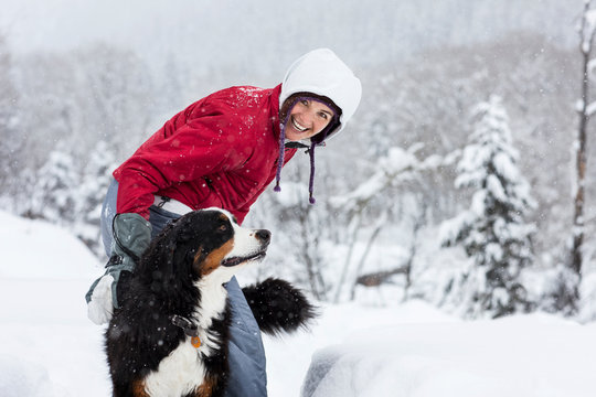 Portrait of a smiling mid adult woman petting her dog while standing outdoors in the snow.
