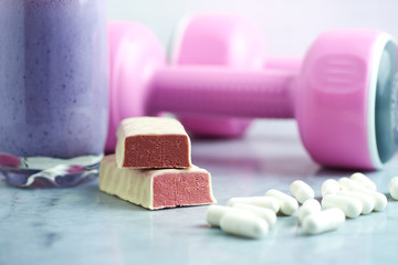 Protein bar in two pieces, Glass of Protein Shake with Milk and Blueberries. Creatine capsules and pink dumbbells in background. Concept for Sport nutrition. Stone / Wooden background. Close up.