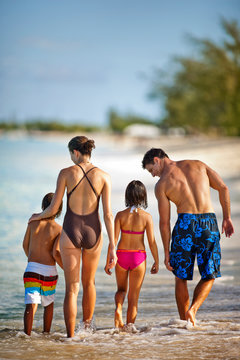 Happy family splashing in shallow water at a tropical beach.