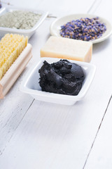 spa products: black mud and clay powder, cosmetic cream, soap, bath salt, shea butter and lavenders on white wood table background
