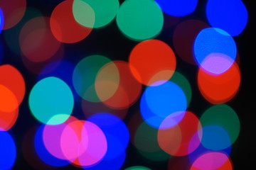 Multi-color blue holiday garland. Garland is blurred. Many big colorful round lights. Fully defocused photo. Blurred background and foreground. Holiday mood. New Year and Christmas is coming.