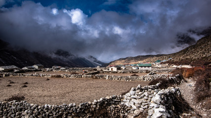 Fototapeta na wymiar Landscape view of the village in a high mountain with many stone houses and enclosed fields. Cloudy sky, daylight. Sagarmatha (Everest) National Park, Nepal.