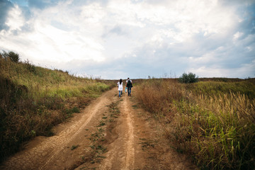 Young family with a small kid walking on the country road back view, outdoors background