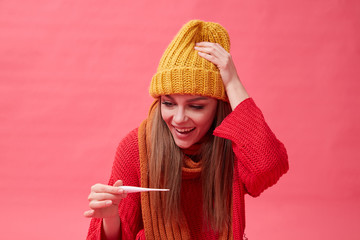Recovering girl holding pills and a thermometer. Red background.