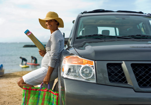 Woman leaning against car holding beach gear.