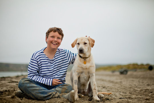 Happy boy sitting on a sandy beach with his dog.